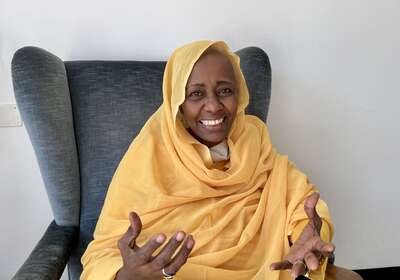 Die Sudanesin Rabab Baldo sitzt in einem Sessel, lächelt und gestikuliert